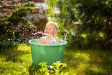 Baby girl flop in a green basin with water on home backyard in summer time