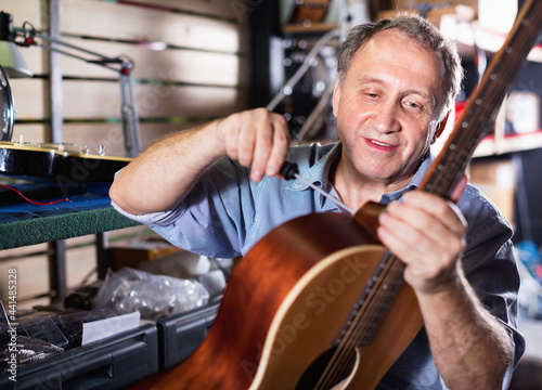 Adult glad cheerful positive music master is repairing music instruments in workshop.