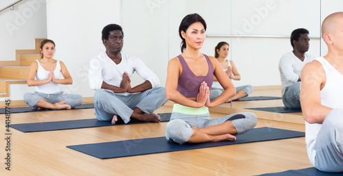 Young men and women maintaining healthy lifestyle practicing meditation in yoga studio