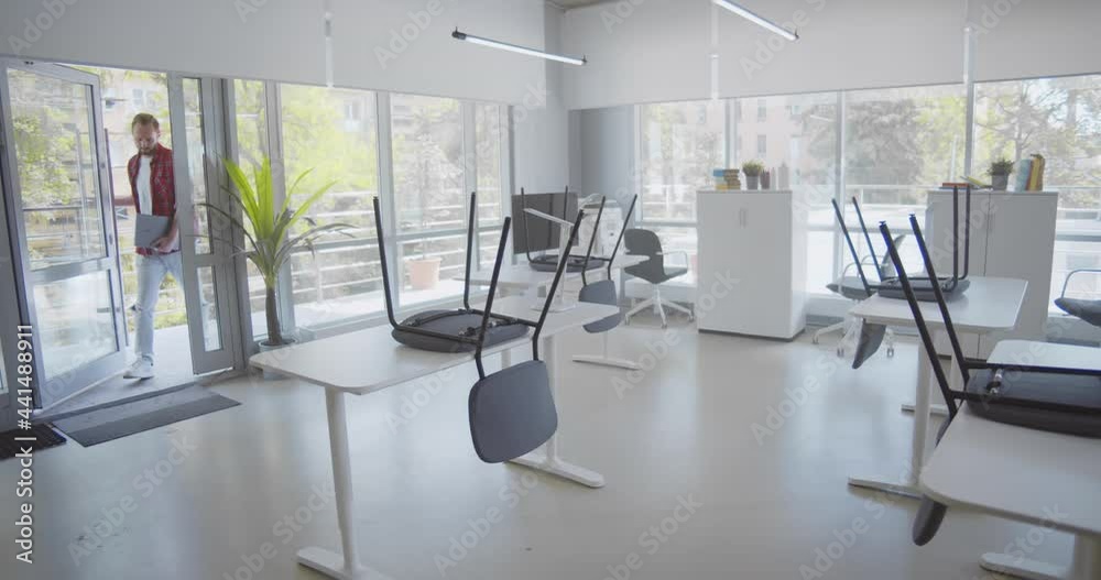 Young male employee entering empty office in morning putting chairs down