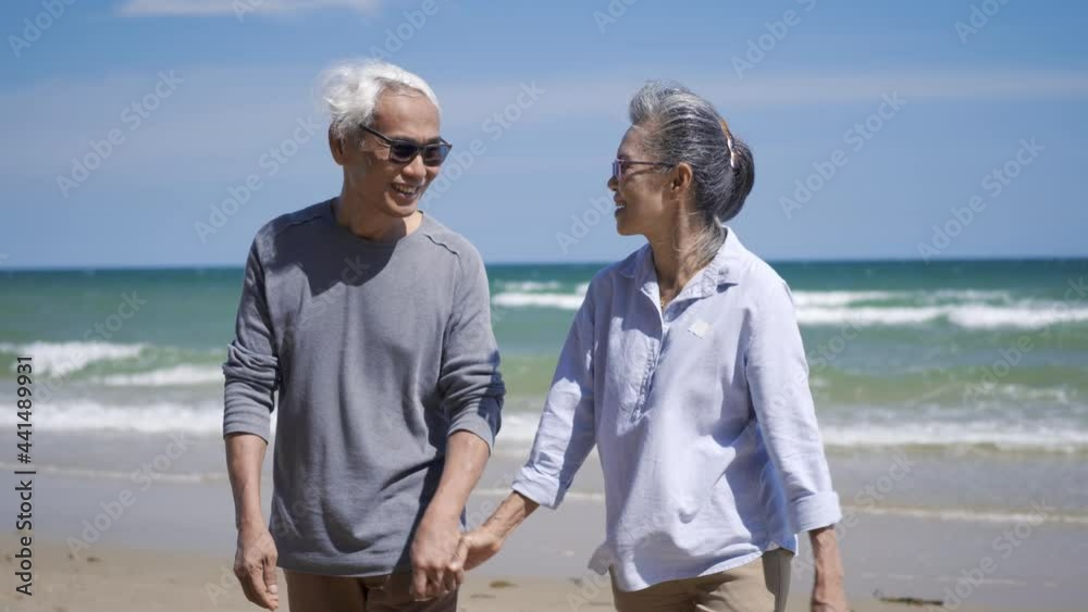 Happy Asian senior man and woman couple holding hands walking from the beach sunny with bright blue sky, Romantic elderly enjoy Travel summer vacation, plan life insurance at retirement couple concept Happy Asian senior man and woman couple holding hands walking from the beach sunny with bright blue sky, Romantic elderly enjoy Travel summer vacation, plan life insurance at retirement couple concept