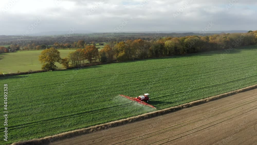 A circling aerial shot of a farming tractor spraying a field with sprayer, herbicides and pesticides on a rural farm.