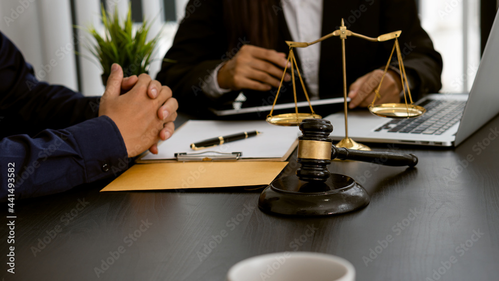 Lawyer discussing contract documents sitting at a desk at the office Legal concepts, advice, legal advisory services and scales with a judge's hammer put forward. Lawyer discussing contract documents sitting at a desk at the office Legal concepts, advice, legal advisory services and scales with a judge's hammer put forward.