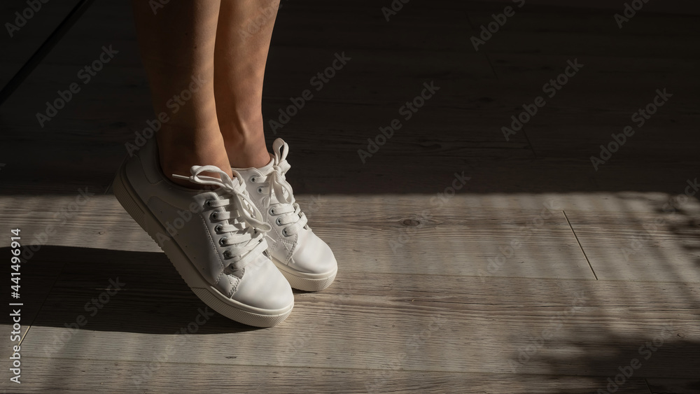 Close-up of female legs in white leather sneakers.