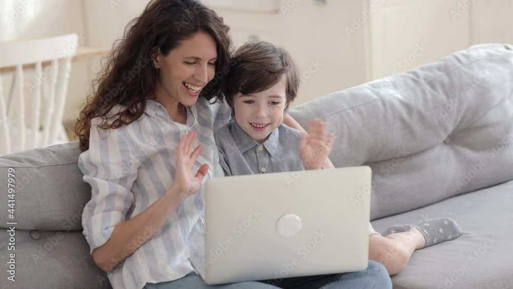 Happy mother with cute preschool son sit on sofa make video call using laptop web cam wave hands to camera. Cheerful mum and kid communicate with grandparents or dad remotely online in conference chat Happy mother with cute preschool son sit on sofa make video call using laptop web cam wave hands to camera. Cheerful mum and kid communicate with grandparents or dad remotely online in conference chat