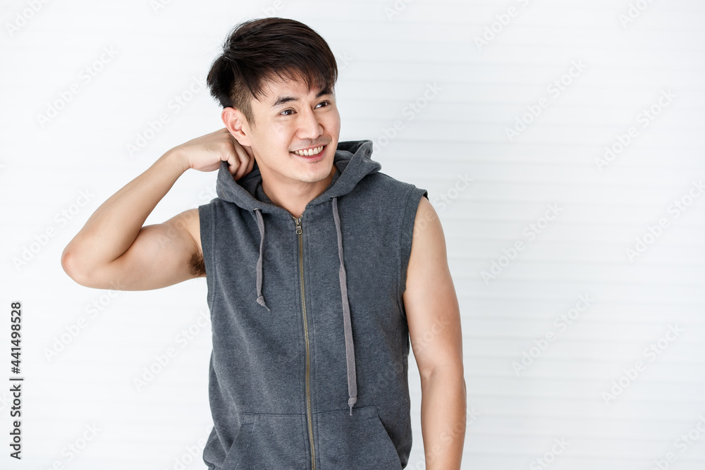 Young Asian happpy handsome smiling man holding hand holding a shirt wearing sleeveless t-shirt gray sportswear in white background. Young Asian happpy handsome smiling man holding hand holding a shirt wearing sleeveless t-shirt gray sportswear in white background.