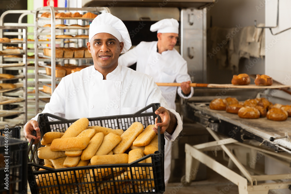 man in chefs uniform with bread in tray in bakery