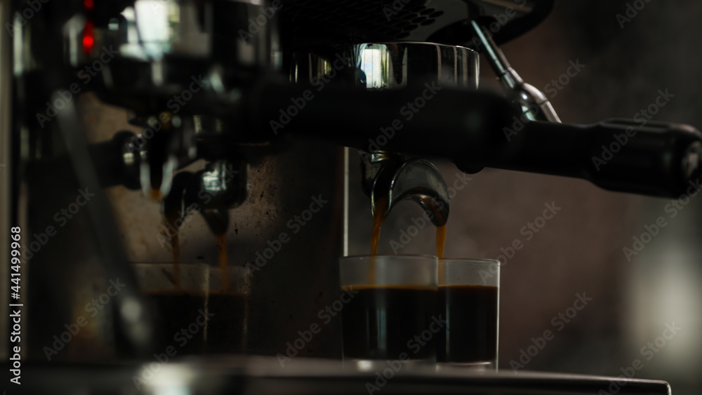 Close up shot of measuring glass filling with dark brown hot delicious good smell coffee by luxury clean steel coffee making machine in cafe with blurred background