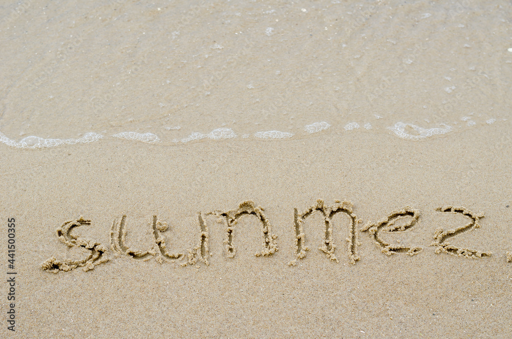 Fototapeta premium The word SUMMER on the yellow sand. Handwritten word on a wet sandy beach. View from above at an angle.