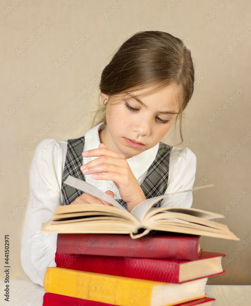 schoolgirl sitting at a table with a stack of books and reading a book close-up schoolgirl sitting at a table with a stack of books and reading a book close-up