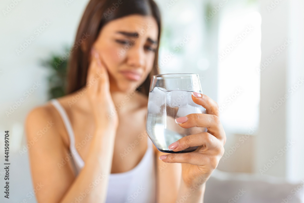 Young woman with sensitive teeth and hand holding glass of cold water with ice. Healthcare concept. woman drinking cold drink, glass full of ice cubes and feels toothache, pain Young woman with sensitive teeth and hand holding glass of cold water with ice. Healthcare concept. woman drinking cold drink, glass full of ice cubes and feels toothache, pain