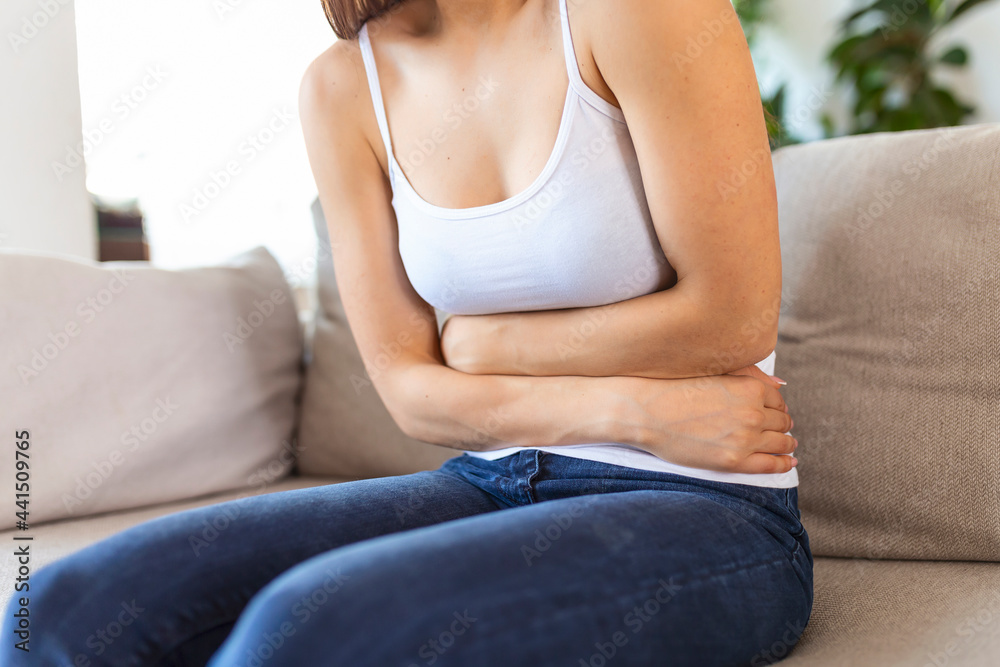 Woman lying on sofa looking sick in the living room. Beautiful young woman lying on bed and holding hands on her stomach. Woman having painful stomachache on bed, Menstrual period