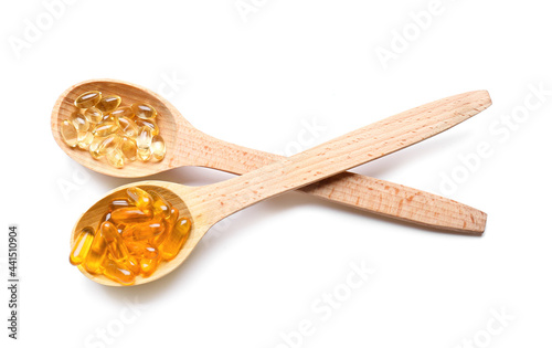 Wooden spoons with fish oil pills on white background