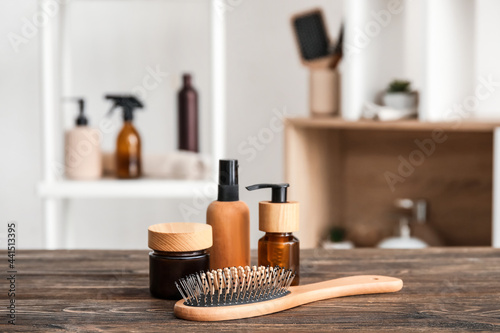 Hair brush and bottles of cosmetic products on wooden table in room