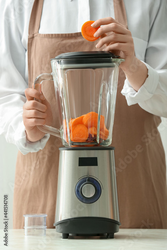 Woman preparing tasty carrot smoothie in kitchen photo