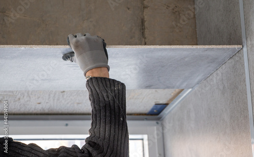 process of installing drywall on concrete surfaces in room with hands of worker in protective gloves. sheathing with gypsum fiber sheets of interior of the room.