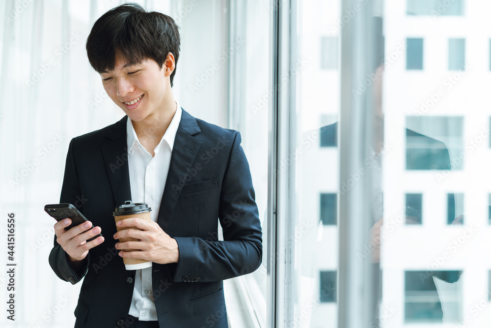 Young businessman in suit drinking coffee and using phone by the window Young businessman in suit drinking coffee and using phone by the window