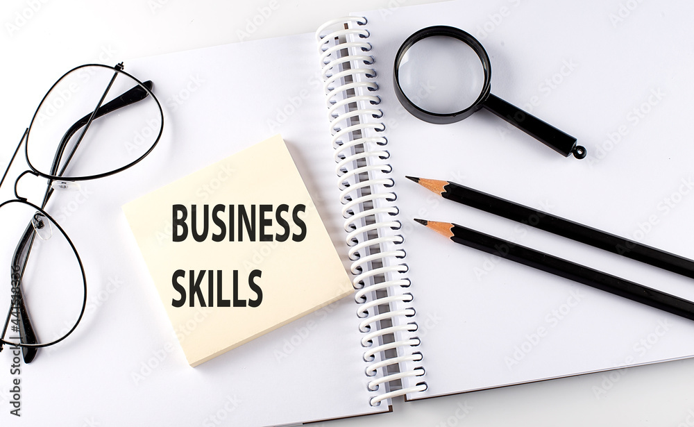 Word BUSINESS SKILLS on the sicker on the notebook with pencils,magnifier and glasses Word BUSINESS SKILLS on the sicker on the notebook with pencils,magnifier and glasses