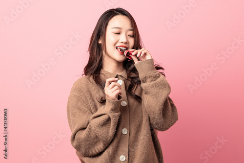 Beautiful woman eating chocolate on pink background