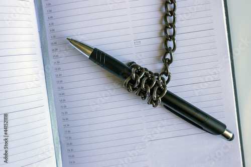 A pen wrapped in an iron chain lies on an empty notebook. Concept- restriction of freedom of speech. photo