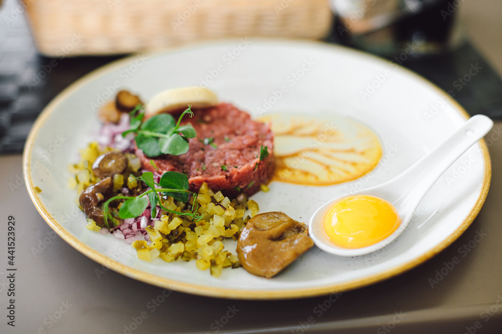 Traditional appetizer with tartare and egg and fresh vegetables on plate in restaurant. Concept of delicious and healthy food. Enjoy your food. Beautiful moments.