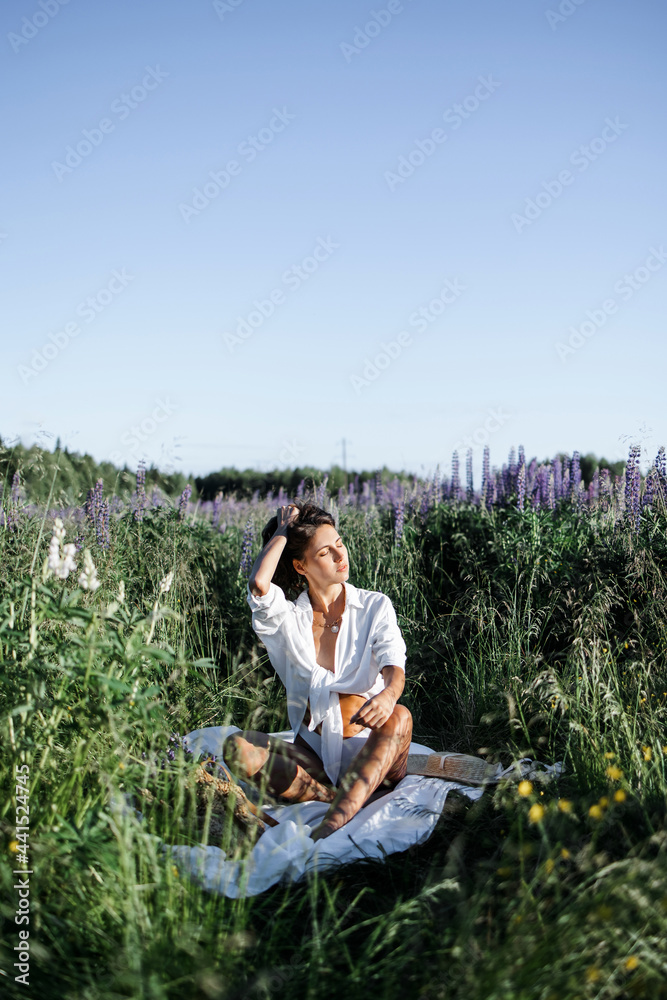 portrait of a sexy girl in a straw hat. A fashionable Caucasian woman in a stylish white shirt feels free in a field with purple flowers in the sun. Lupine field in summer. The concept of a summer cou