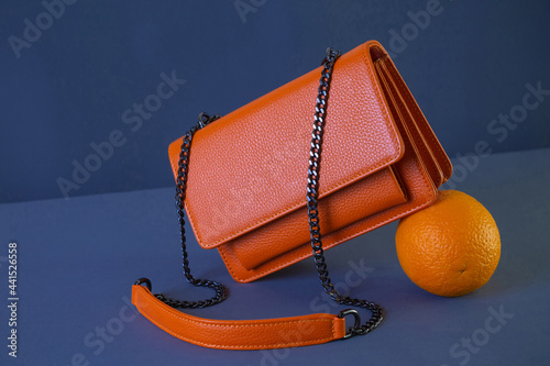 Bright orange leather women's handbag and orange fruit on dark fabric background. Fashion and shopping concept
