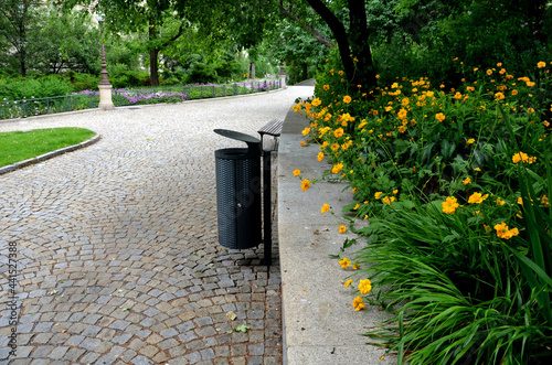 bench at a retaining wall in a park of black bushes early spring perennials on a high flowerbed path of granite cubes
 photo