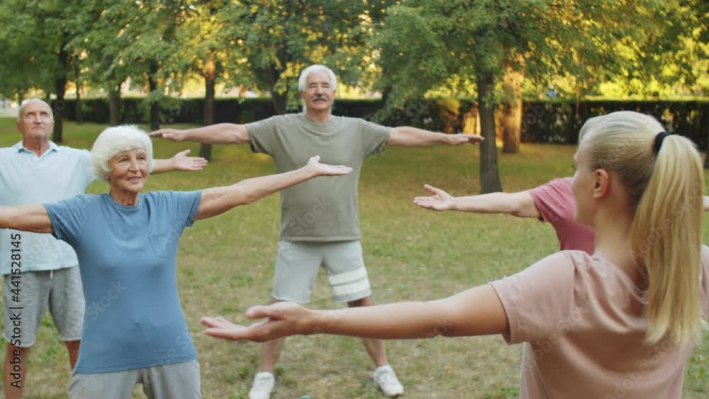Group of senior men and women in sportswear exercising in park with female fitness instructor