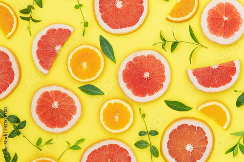 Summer bright background with oranges, grapefruits and green leaves on the yellow surface 