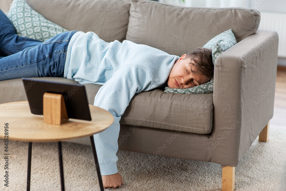 people, boredom and depression concept - bored or lazy young man with tablet pc computer lying on sofa at home