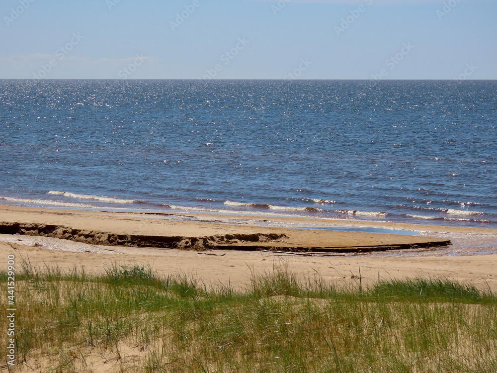 Sand dunes by the Baltic sea: blue sky and sea, white waves, yellow sand, green harsh grass
