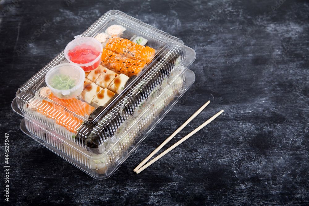 Two plastic boxes with sets of rolls, wasabi and ginger, bamboo chopsticks on a black background. Two plastic boxes with sets of rolls, wasabi and ginger, bamboo chopsticks on a black background.