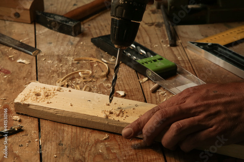 Carpenter using drill machine to make a hole on wooden plank. DIY, woodworking project.