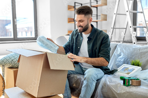 Tableau sur toile moving, people and real estate concept - happy smiling man unpacking boxes at ne