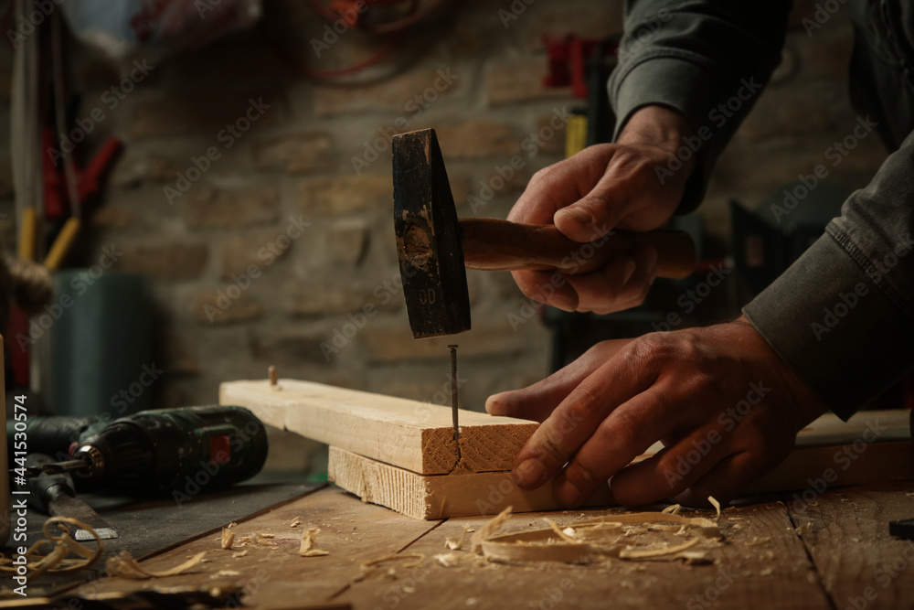 Carpenter hammering nail into wooden plank in workshop. Carpenter hammering nail into wooden plank in workshop.