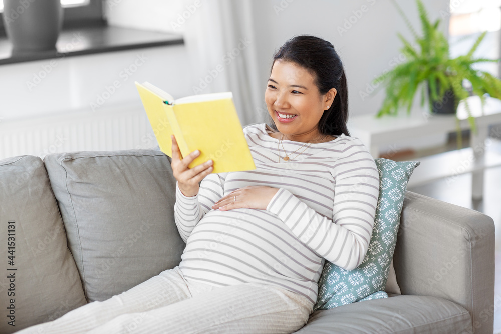 pregnancy, people and leisure concept - happy smiling pregnant asian woman sitting on sofa and reading book at home pregnancy, people and leisure concept - happy smiling pregnant asian woman sitting on sofa and reading book at home