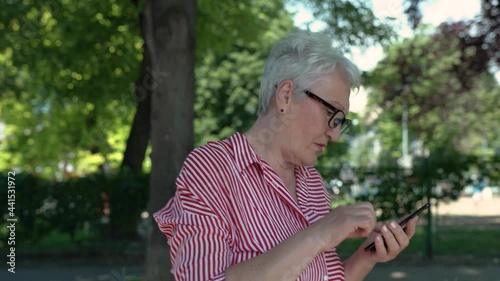 Portrait of senior woman in the park walking while texting.