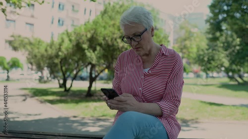 Portrait of senior woman in a park smiling while texting.