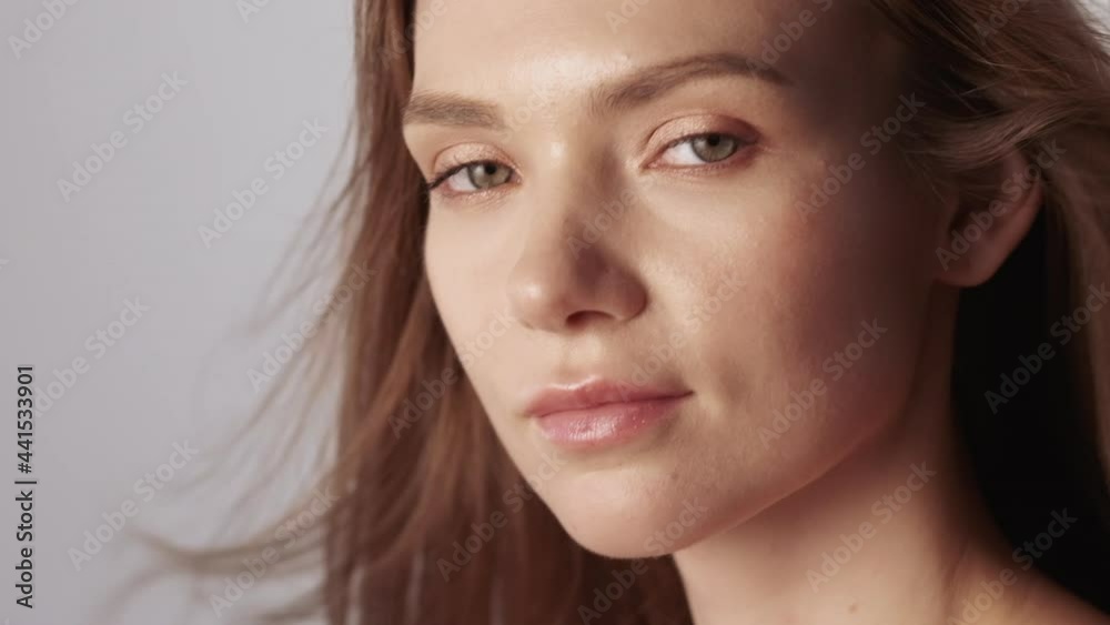 Nude makeup face. Organic cosmetics. Facial skincare. Wellness health. Relaxed woman with flying brown hair perfect radiant skin isolated on gray. Nude makeup face. Organic cosmetics. Facial skincare. Wellness health. Relaxed woman with flying brown hair perfect radiant skin isolated on gray.