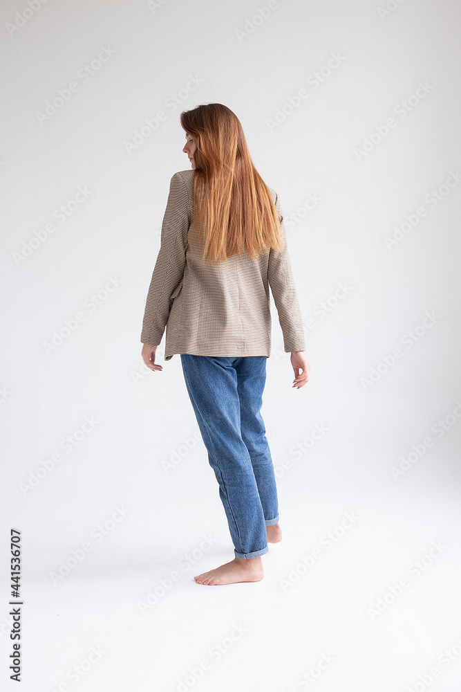 portrait of young caucasian attractive woman with long brown hair in blue jeans and suit jacket on white background. skinny pretty lady posing at studio with bare feet portrait of young caucasian attractive woman with long brown hair in blue jeans and suit jacket on white background. skinny pretty lady posing at studio with bare feet