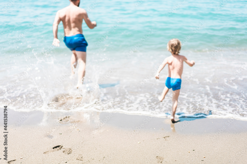 Father and son running towards the ocean together during summer vacation, blurred Father and son running towards the ocean together during summer vacation, blurred