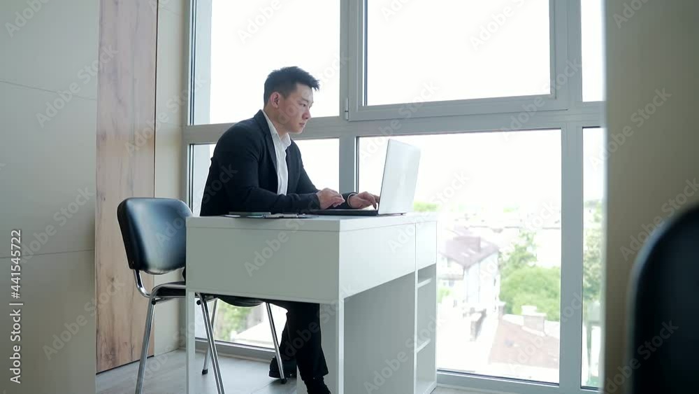 silhouette of a business Asian man sitting and working at a computer or laptop at work in the office. Male Manager working online alone in overtime in front of a window overlooking the city silhouette of a business Asian man sitting and working at a computer or laptop at work in the office. Male Manager working online alone in overtime in front of a window overlooking the city