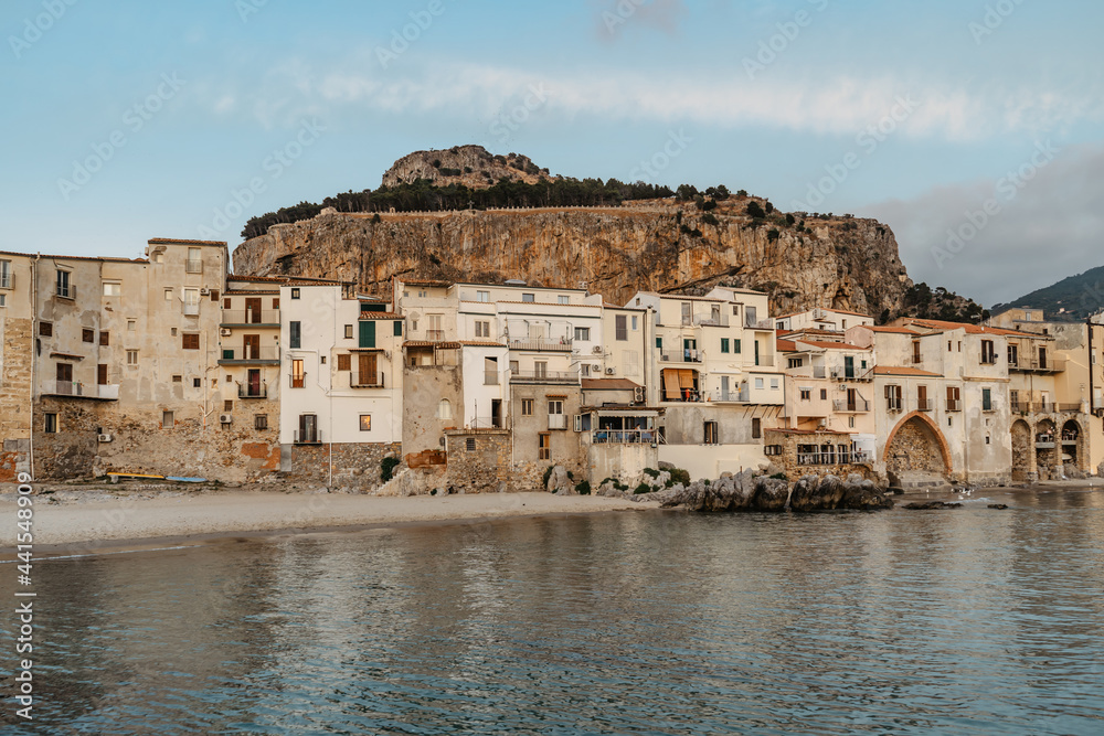 Sunrise on beach in Cefalu, Sicily, Italy, old town panoramic view with colorful waterfront houses, sea and La Rocca cliff.Attractive summer cityscape,traveling concept background.Italian vacation.