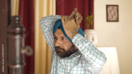 Portrait of a bold Indian Punjabi man fixing his blue turban with a long steel hairpin. A handsome Sikh gentleman adjusting his turban and hair properly with a long hairpin showing his faith toward... photo