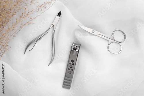 Manicure scissors, nail clipper and cuticle nippers on white fabric, flat lay