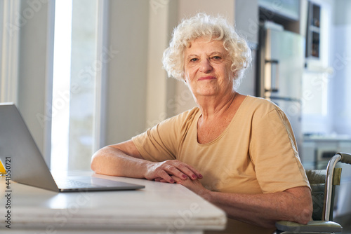 Confident elderly woman sitting at laptop computer at home