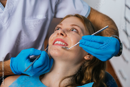 A smiling young woman sits in a dentist s chair while the doctor examines her teeth.