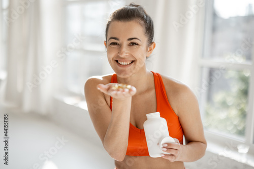 фотографія Portrait of a cheerful woman taking supplements or vitamins in the form of capsules after training in the gym