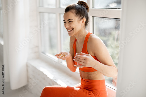 Happy woman takes supplements or vitamins in the form of capsules after training in the gym. Concept of additional nutrition during training photo